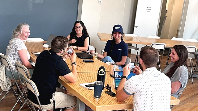 A group of entrepreneurs and business owners gathered around a table at Route 93 Innovation Hub, laughing and connecting during a networking session.